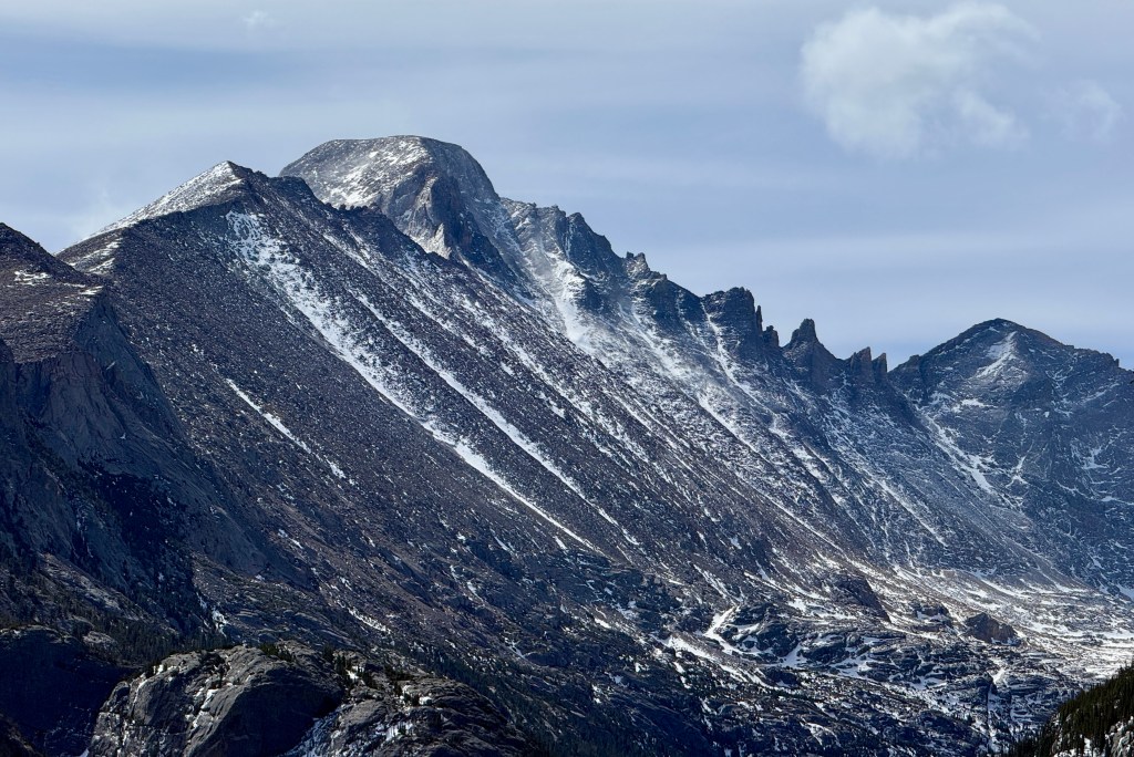 A panoramic view of snow-capped mountains under a cloudy sky, showcasing rugged peaks and steep slopes.