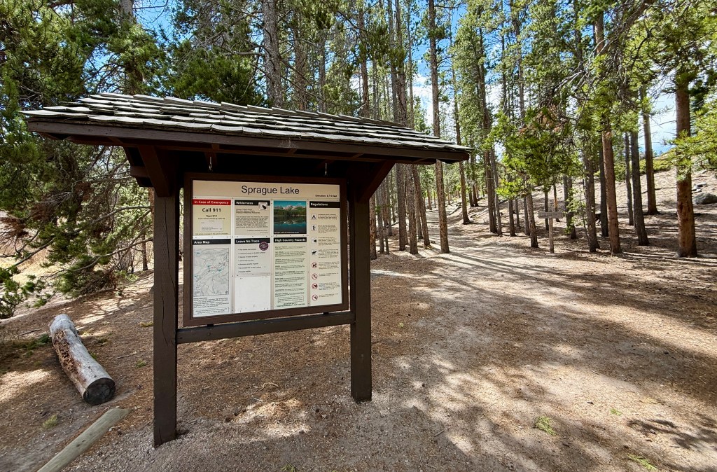 Information sign for Sprague Lake located in a wooded area, featuring maps, regulations, and visitor information.