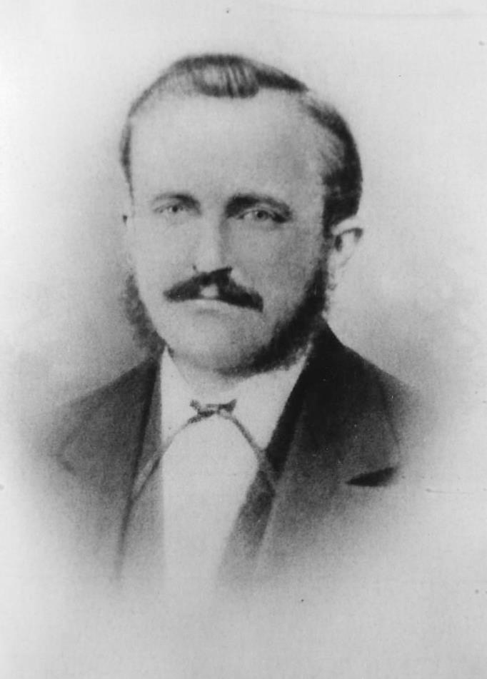 A vintage black and white portrait of a man with a mustache and styled hair, wearing a suit and a tie.