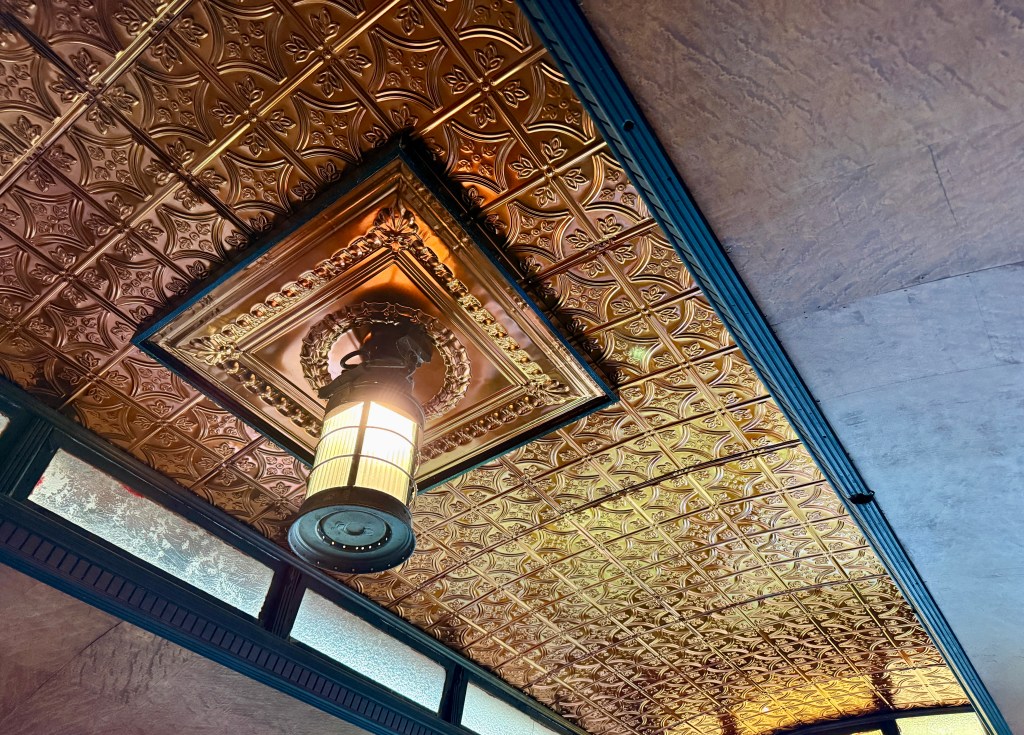 Close-up view of a decorative ceiling with embossed gold panels and an artistic light fixture.