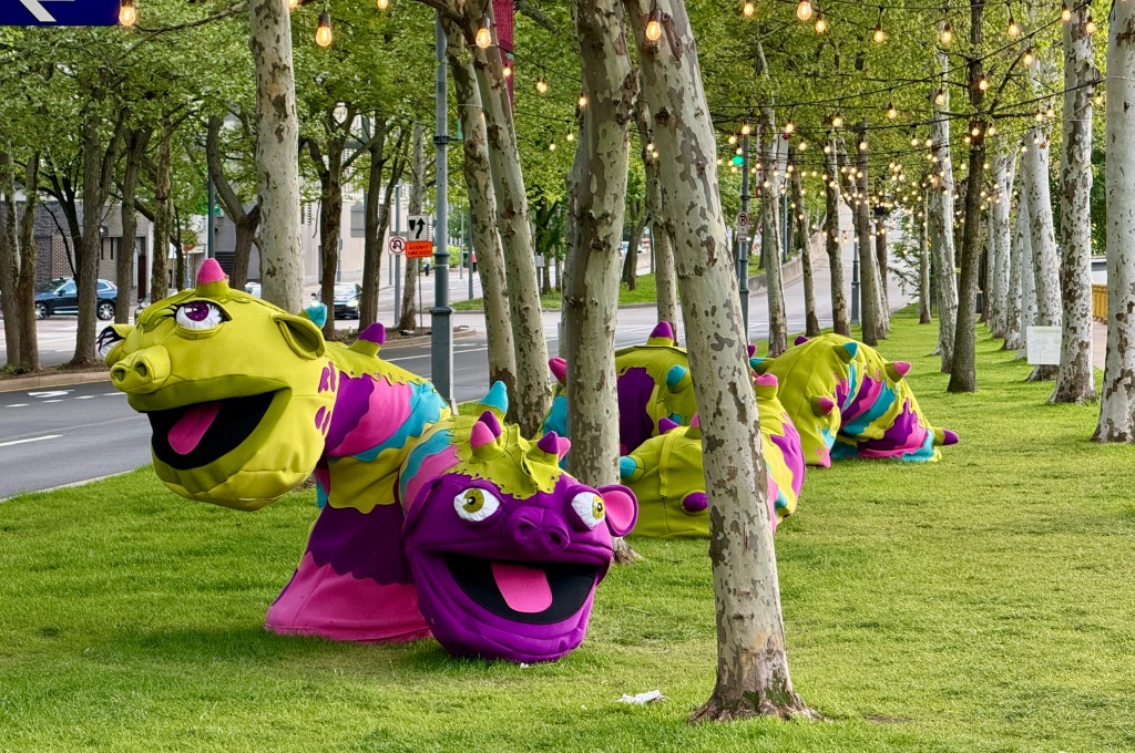 Colorful oversized caterpillar decorations on a grassy area with trees and string lights.
