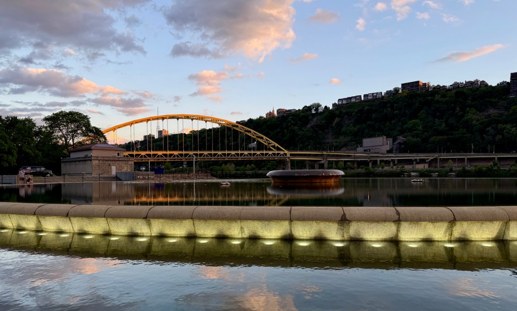 Scenic view of a bridge over a river at sunset, with reflections in the water and a vibrant sky.