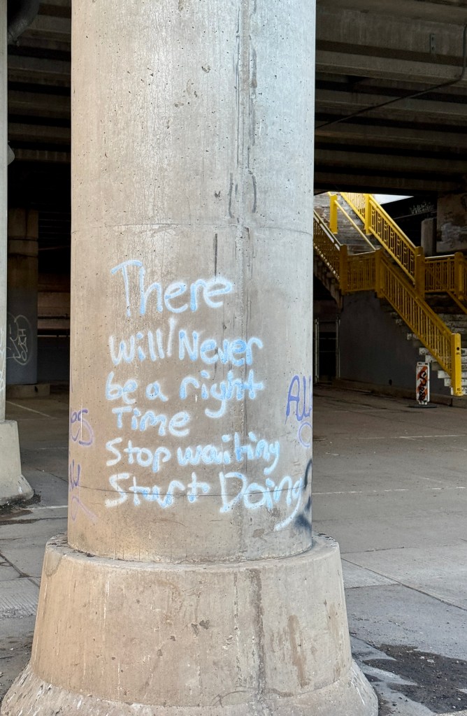 Graffiti on a concrete pillar with motivational text that reads 'There will never be a right time. Stop waiting. Start doing.'