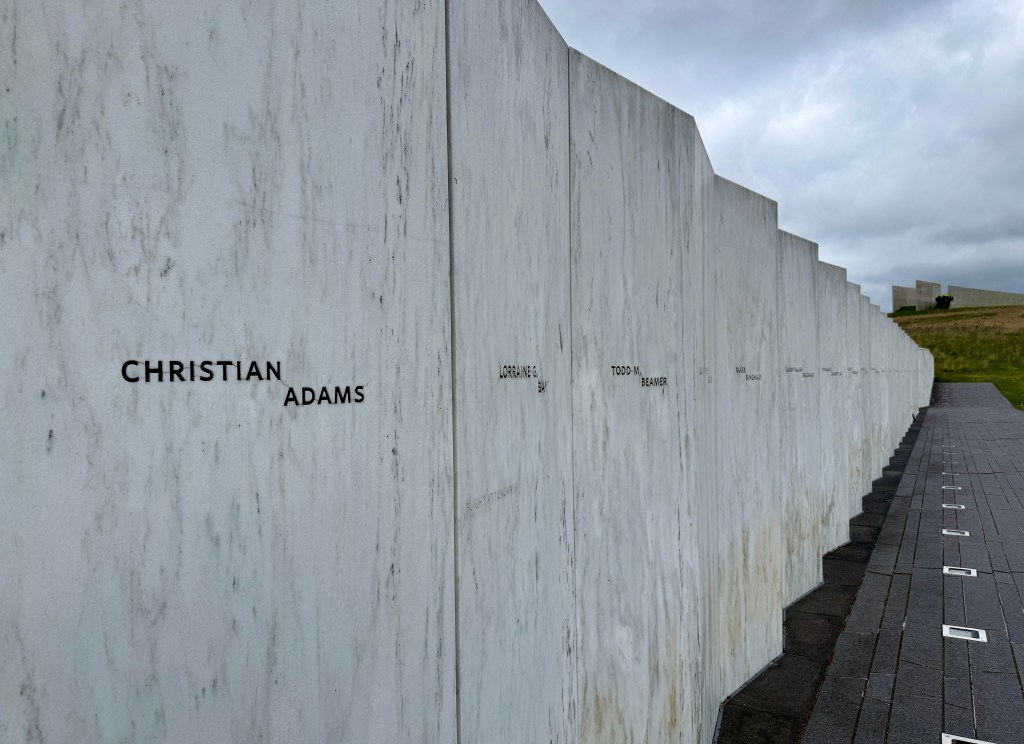 Names engraved on a marble memorial wall in a solemn outdoor setting.