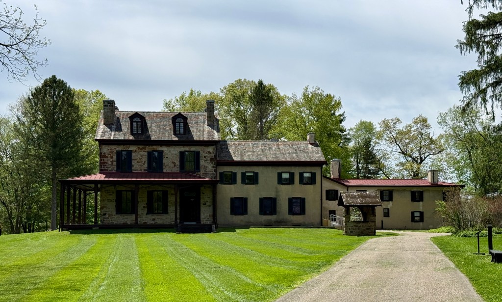 Historic two-story house with a gabled roof and dark shutters, set on a landscaped lawn.