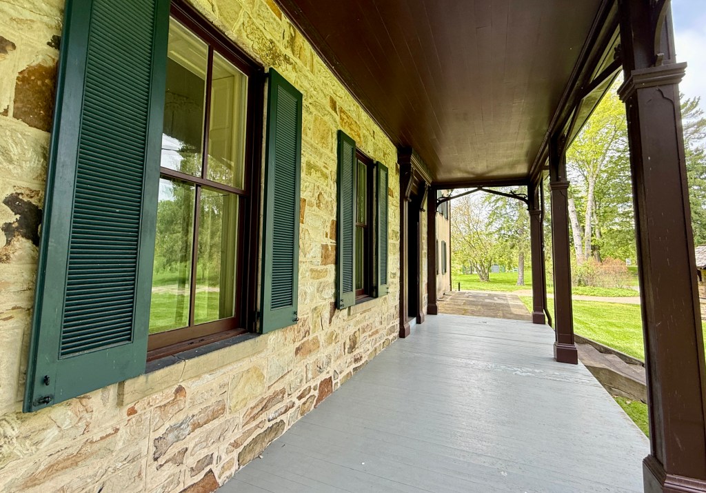 View of a stone building's porch featuring green shutters on the windows and a wooden ceiling.