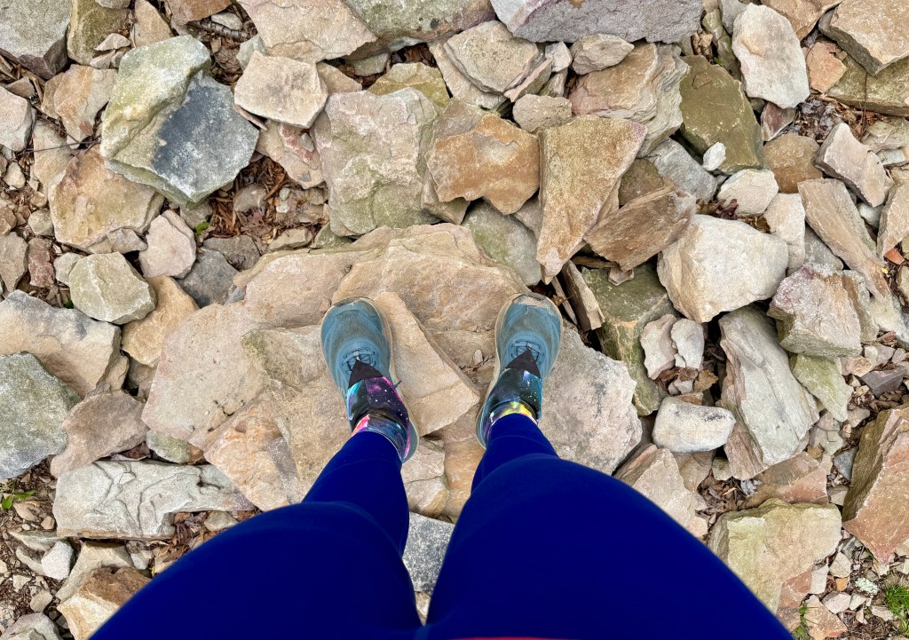 Close-up view of legs wearing blue leggings and hiking boots standing on a rocky terrain.