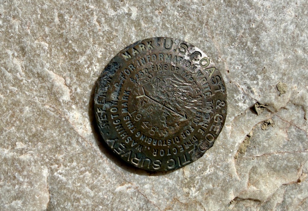 A metal survey marker embedded in a rocky surface, featuring text indicating it belongs to the U.S. Coast and Geodetic Survey, with visible engravings and a date of 1948.