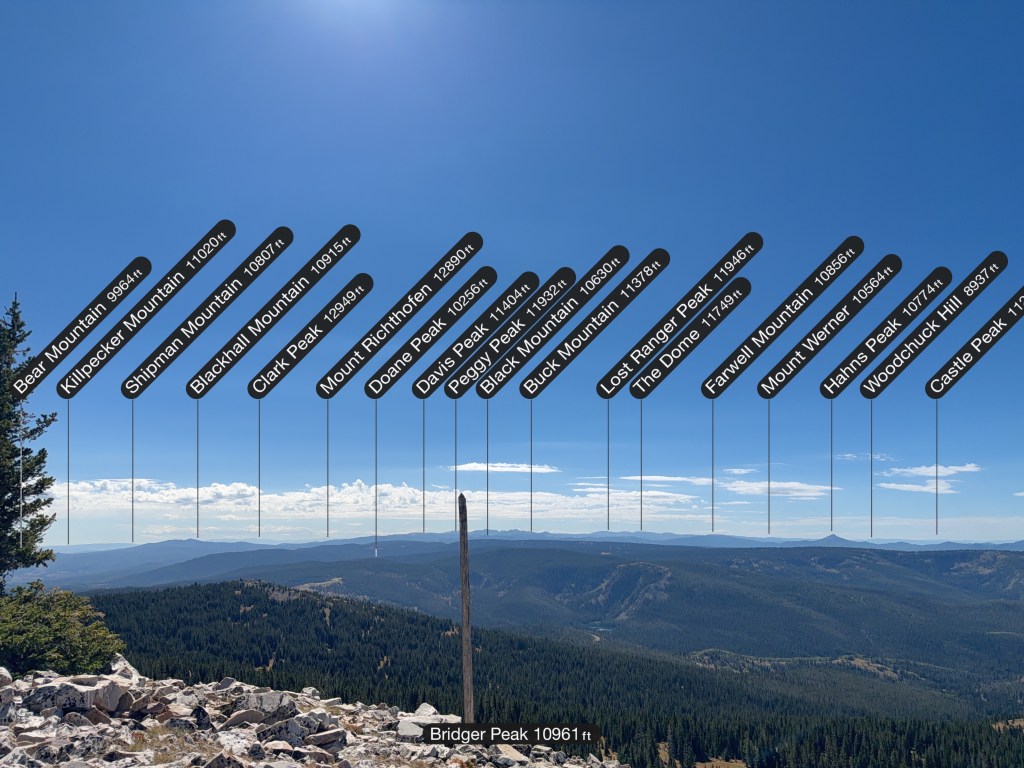 Panoramic view of mountains with labeled peaks and their elevations, including Bridger Peak at 10,961 ft, against a clear blue sky.